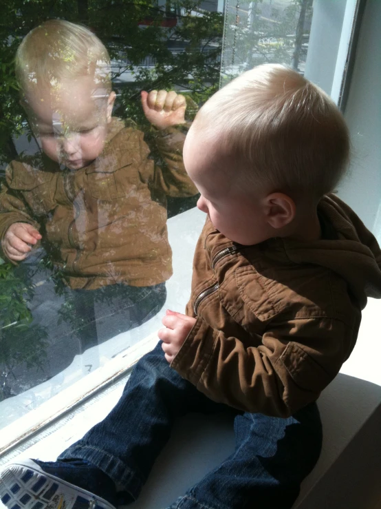 a baby looking out a window at some bushes