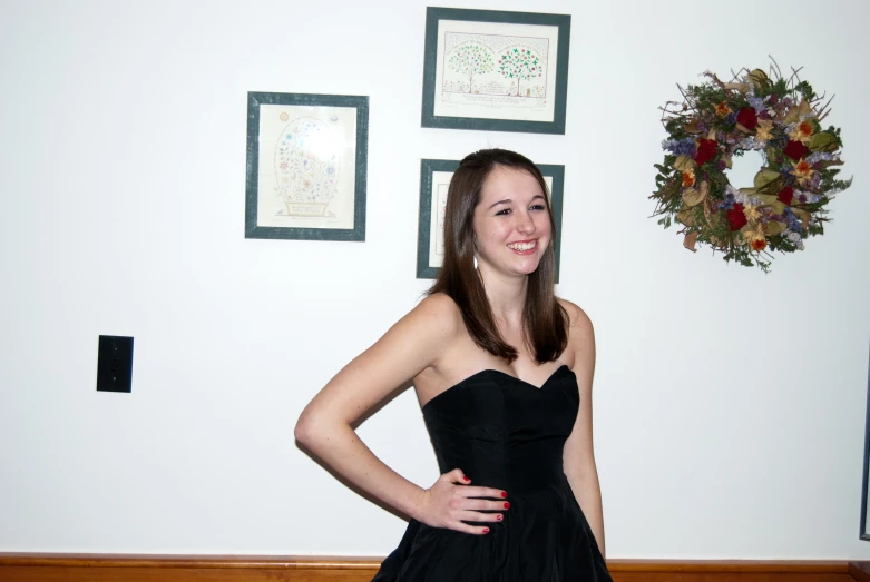 a woman in a black dress smiles in front of a white wall with some framed artwork