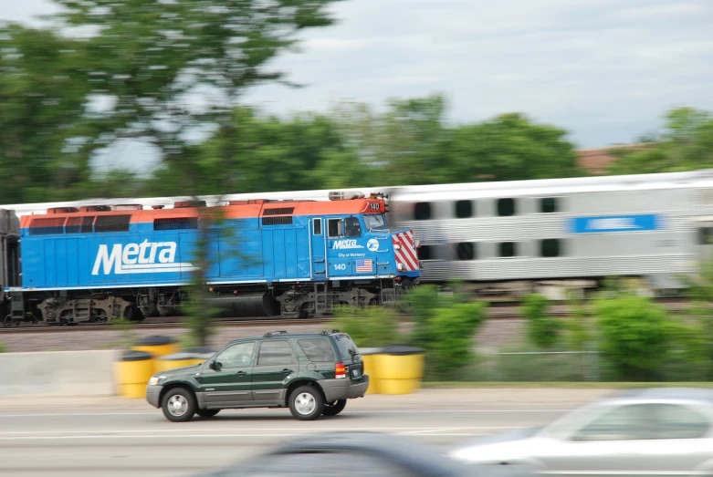 a suv is driving beside a train on the tracks