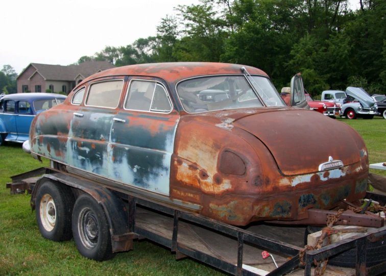 an old rusty car is shown in a trailer on grass