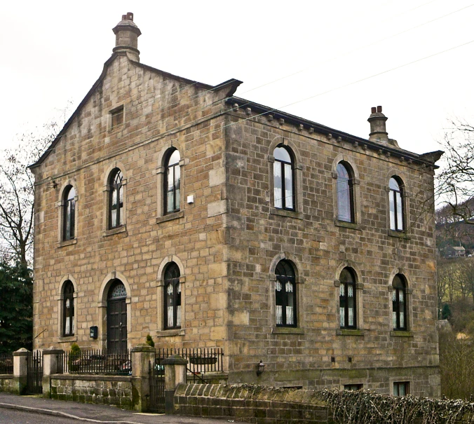 an old stone building with arched windows and a brick fence surrounding it