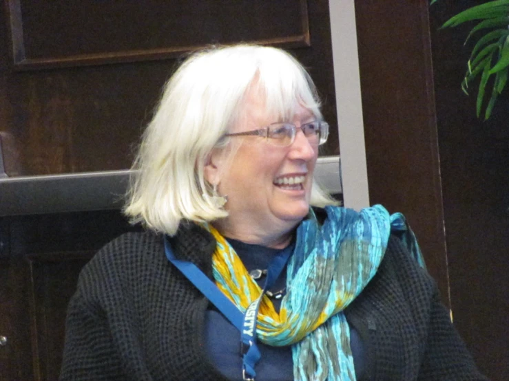 a blonde woman in black shirt and glasses talking to another person