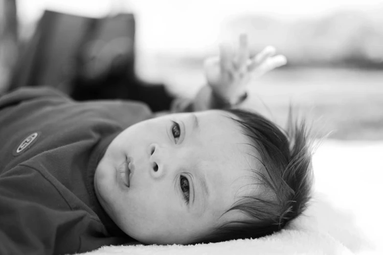 baby lying on blanket and looking at camera with hand reaching for the viewer