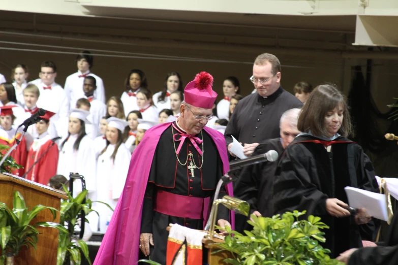 a priest at a graduation speech with two other graduates