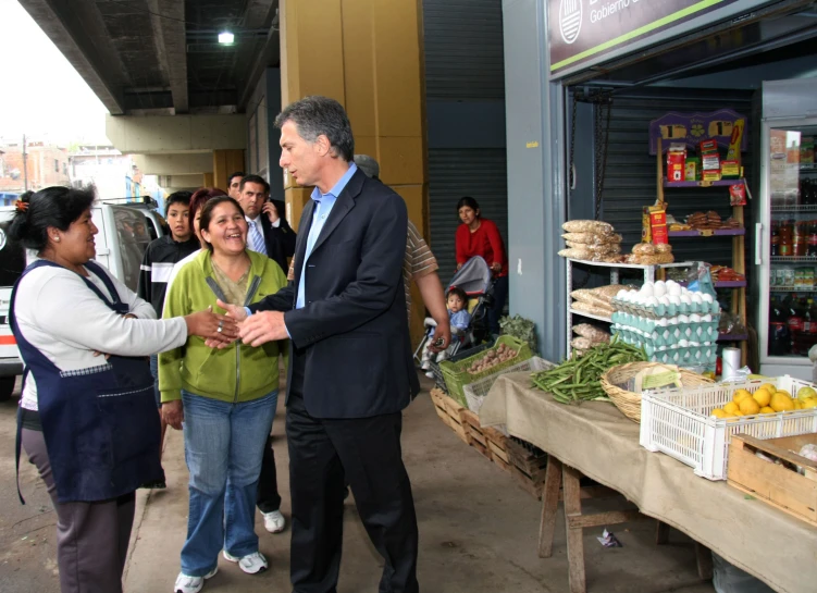 three people stand near tables full of vegetables and produce at an outside market