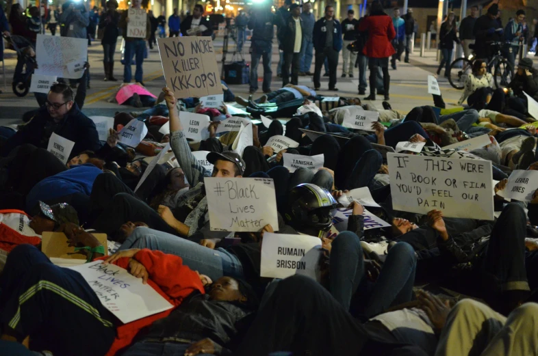 a large group of people are laying in a field and holding signs
