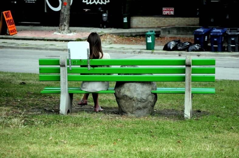 a woman sitting on top of a green wooden bench