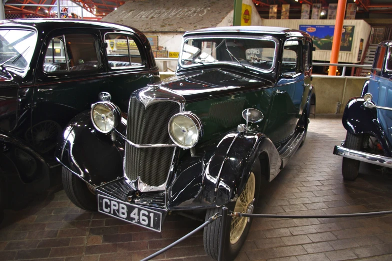 two classic cars in an automobile museum, one is black and the other is white