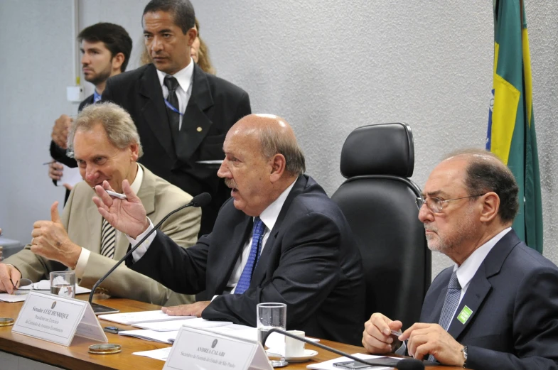 four men sitting at a table and one is speaking