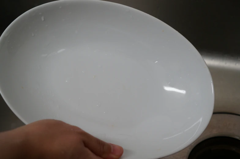 a person's hand holding a white plate in front of a sink