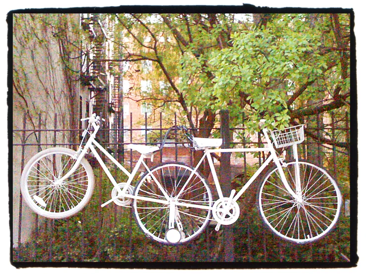 two bicycles with baskets tied to the front of them hanging on a fence