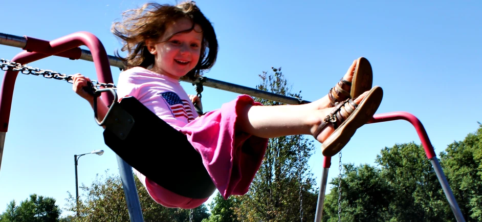 a girl hanging from the top of a pink pole on a metal climbing frame