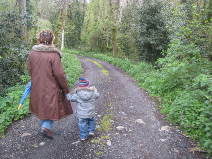 a woman and a child walk down the dirt road