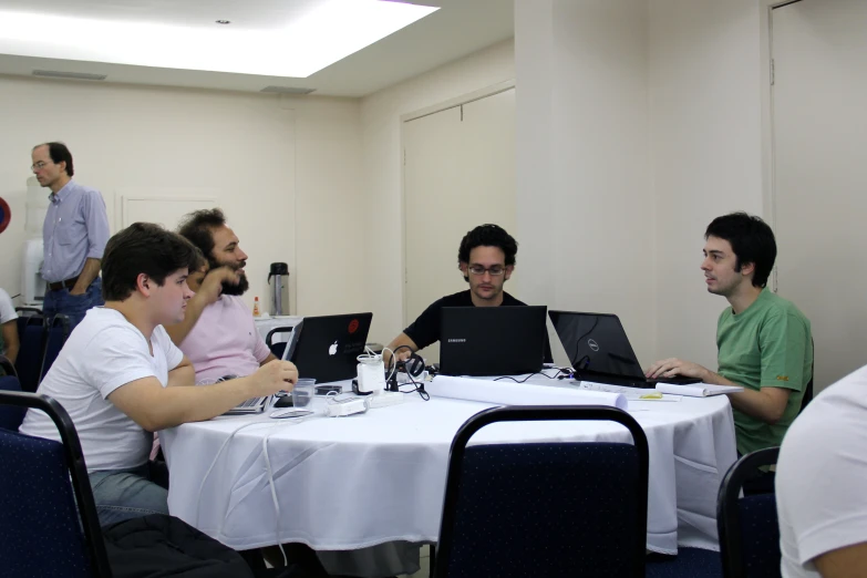 several men sitting at a table with laptop computers