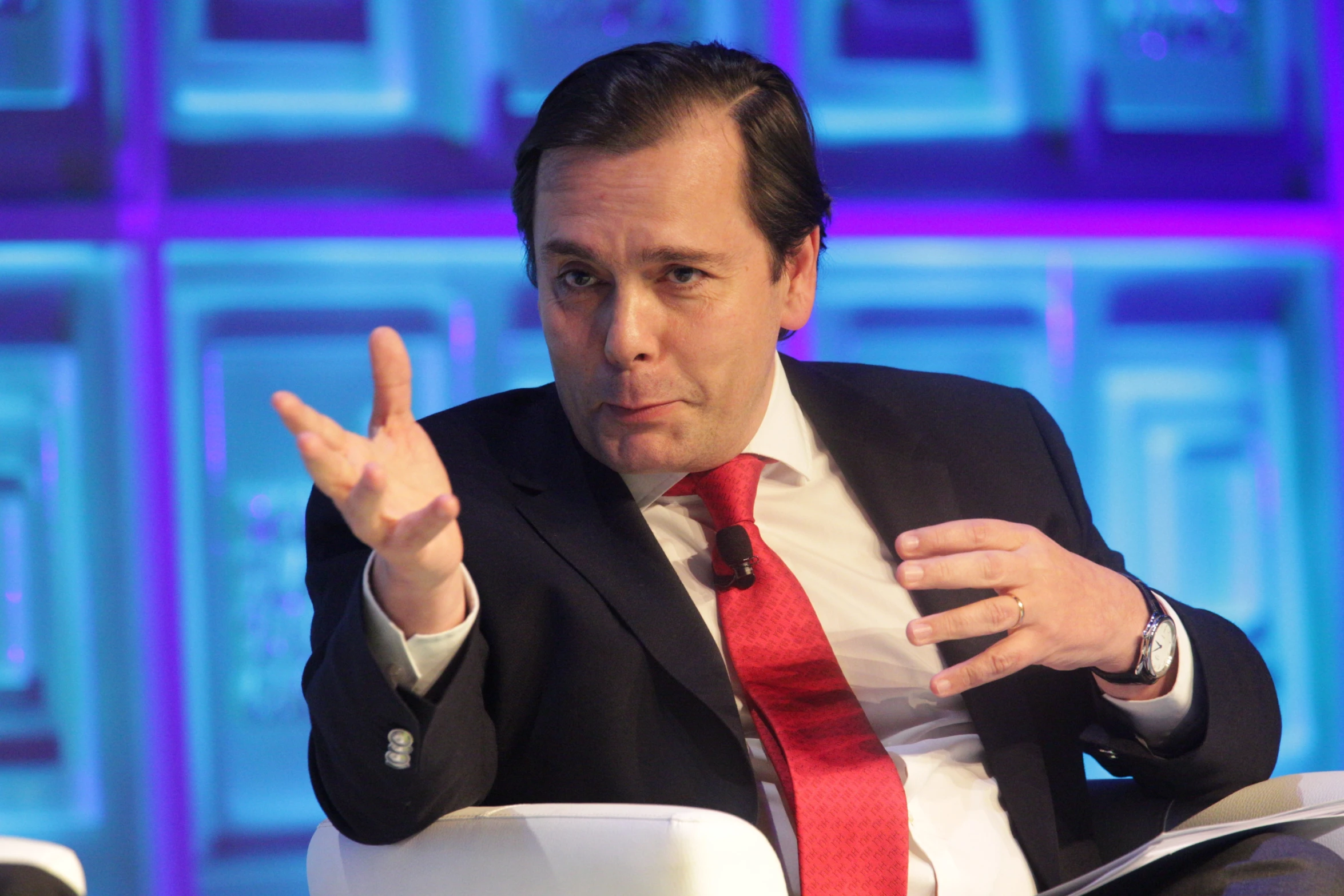 a man in a suit sitting in a chair while holding his finger out