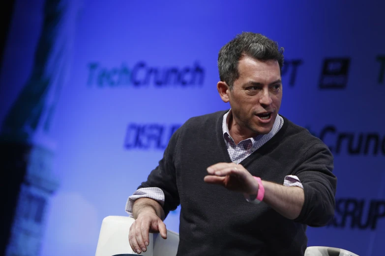 man talking on stage at a conference holding soing in his hand