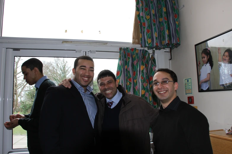 three men pose in a living room while smiling