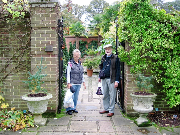 two people standing by the gates of a brick house