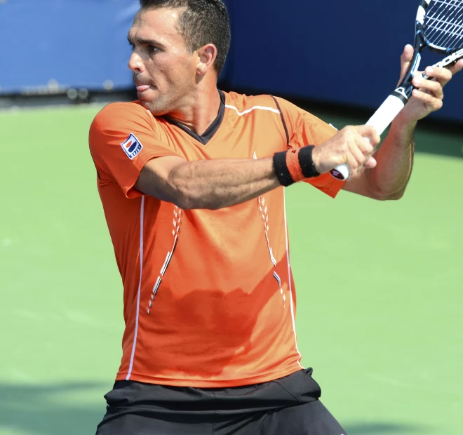 a man in an orange shirt holds his tennis racket back to the camera