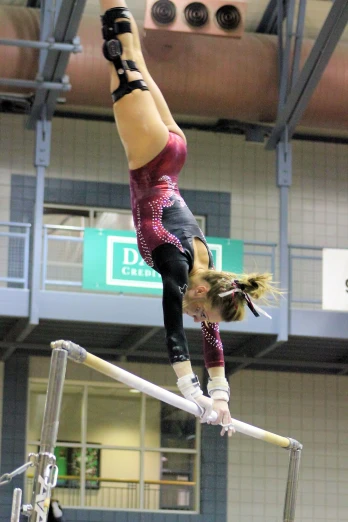an aerial acrobaticist performing on the uneven bars in an indoor gym