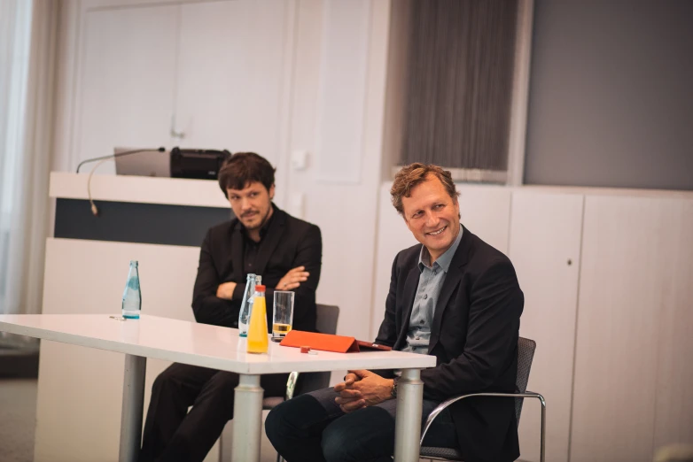 two men sitting at a table in an office