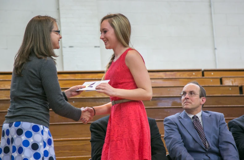 a woman is shaking hands with another woman who is in front of the audience