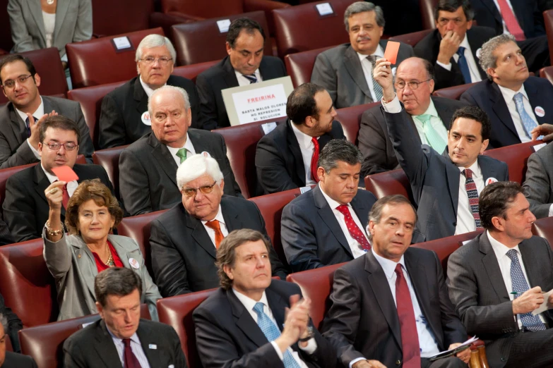 a group of people in suits sitting down with some of them raising their fingers