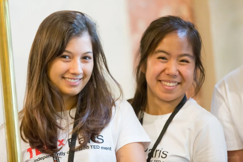 two young women smile as they are looking at soing in the mirror