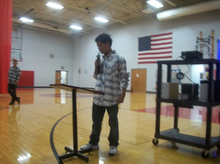 a boy stands in the gym holding his hands up to the microphone