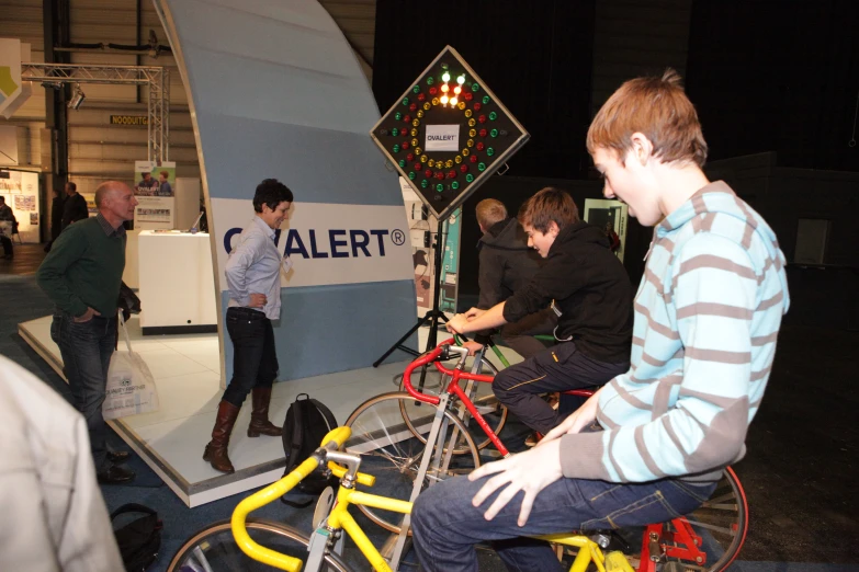 some guys are standing around a display and one man is sitting on a bicycle