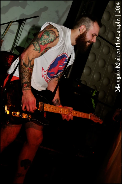 tattooed man holding up his guitar to an audience