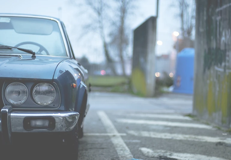 an older car with a big hood sits parked in the street