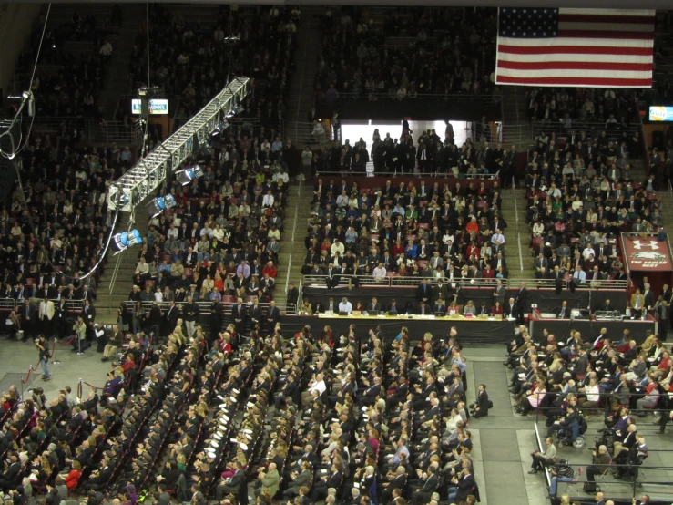 a crowd in a stadium stands in a line for a speech