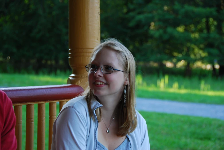 a young woman in glasses is sitting down on a porch