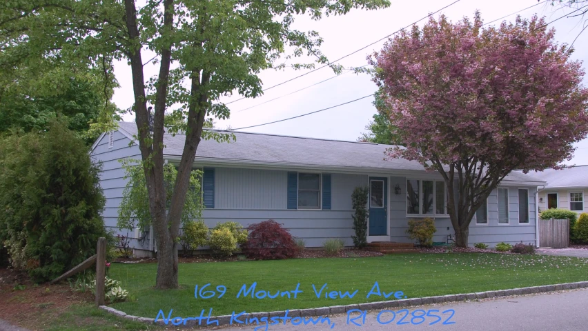 the house is blue and grey with pink flowering trees