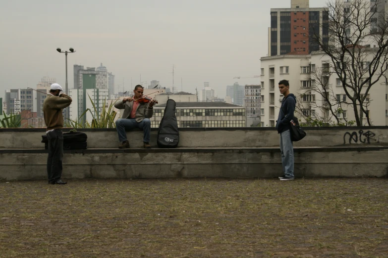 three men sitting on a cement ledge with luggage