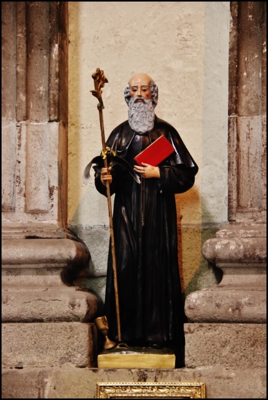 a statue of a man in black clothes holding a book and standing next to pillars