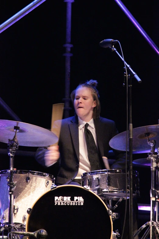 the man is playing drums on stage in front of the microphone