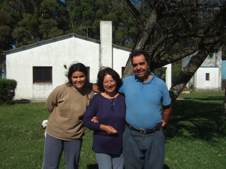 a man and two woman smile as they stand in a grassy area in front of a house