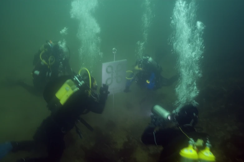 three scubas with helmets and equipment looking up