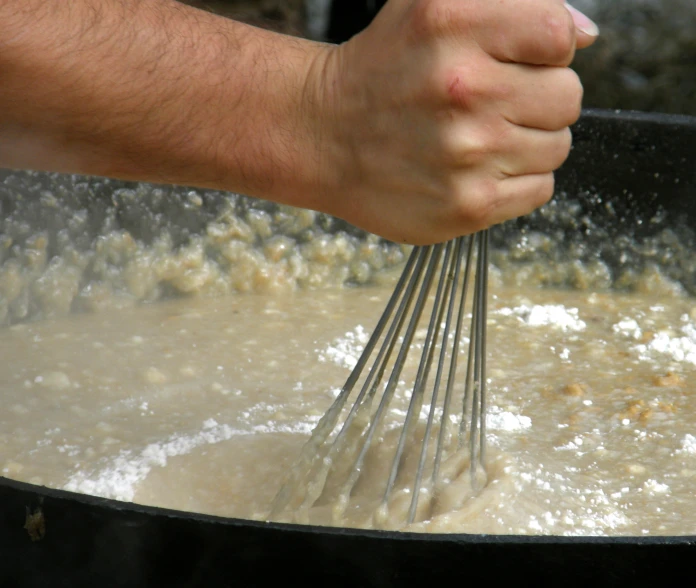 someone's hand holding an iron mixing bowl and whisk mixing ingredients for a meal