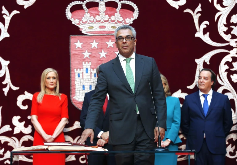 a man wearing a suit and tie standing in front of two men and a woman