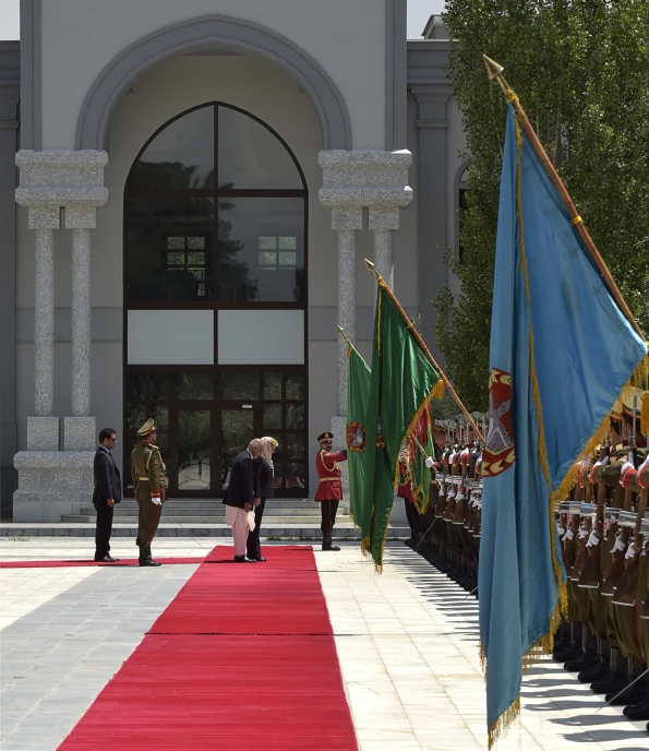 two military men and a woman in military uniforms stand at attention to soldiers with flags