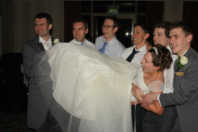 a bride carrying a wedding dress as several men look on