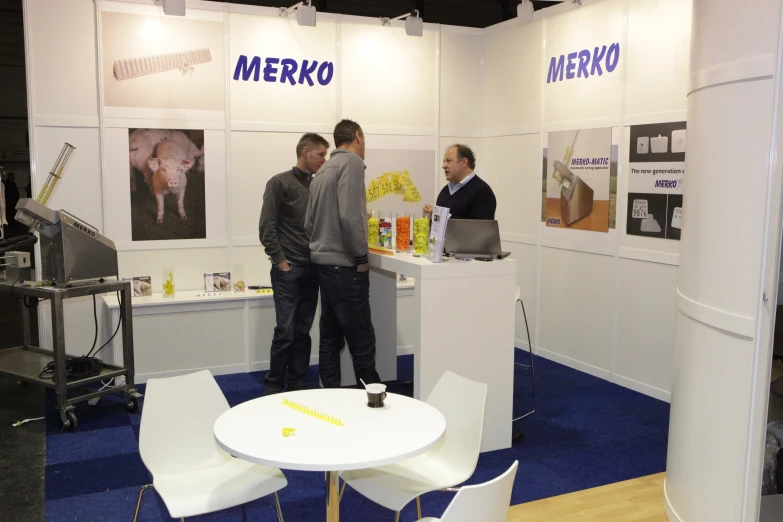 three men are talking in a booth at an exhibition