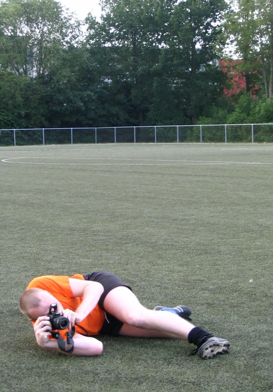 man laying on the ground in a field wearing an orange shirt