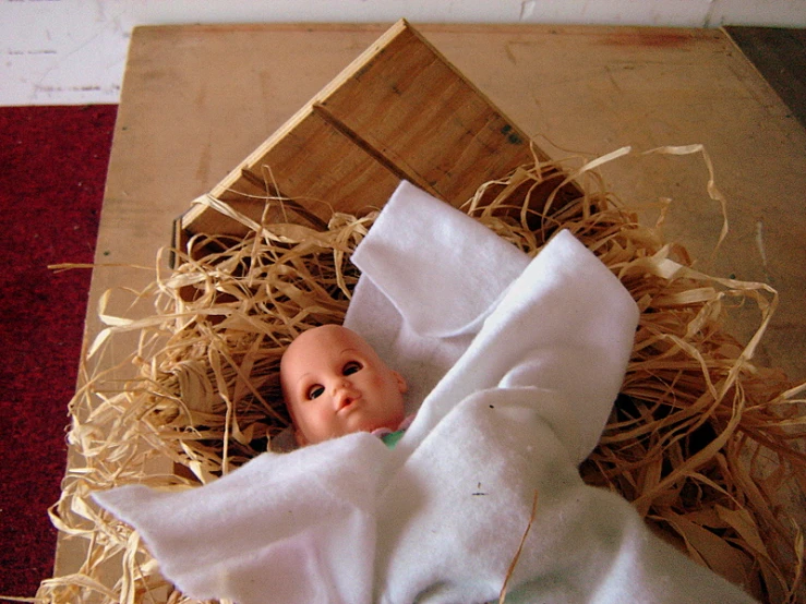 a baby doll is laying on hay in the corner of a basket