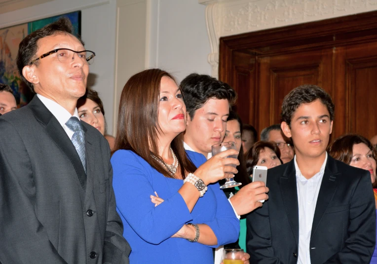 a man in a suit and blue dress holds his drink while looking into the distance