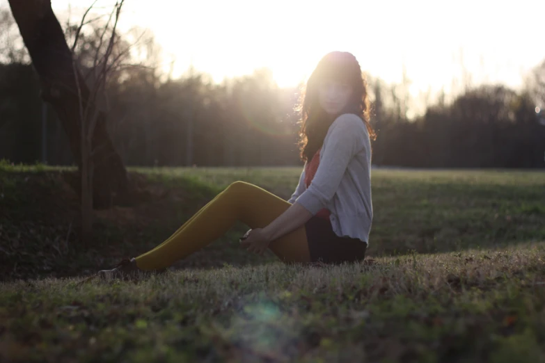 a woman sitting in the grass holding a yellow umbrella