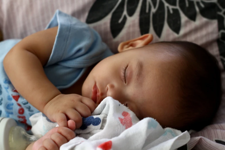 a baby is asleep on the sofa with his hands tucked under his chin